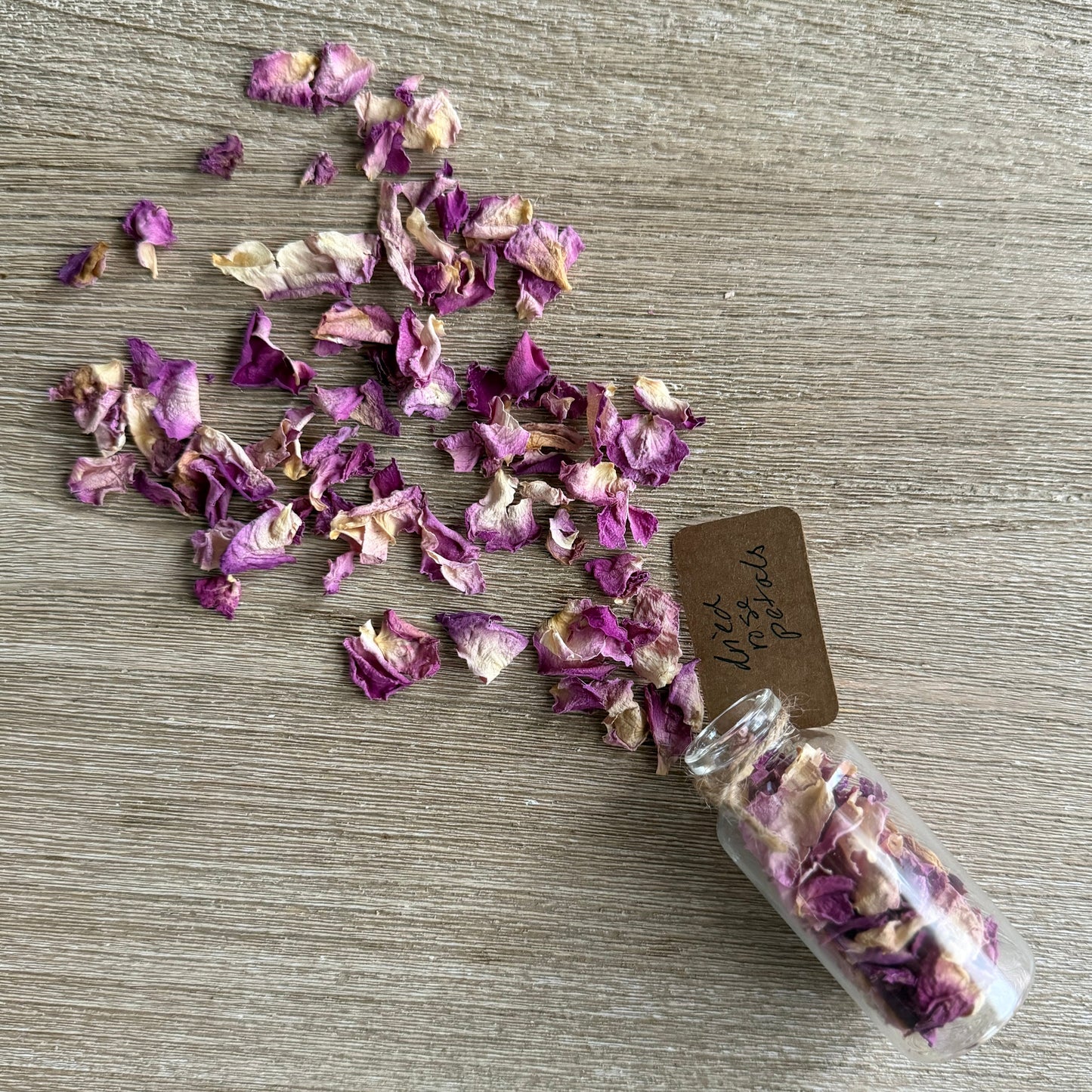 Small glass jar filled with dried purple and white flowers on a wooden surface.