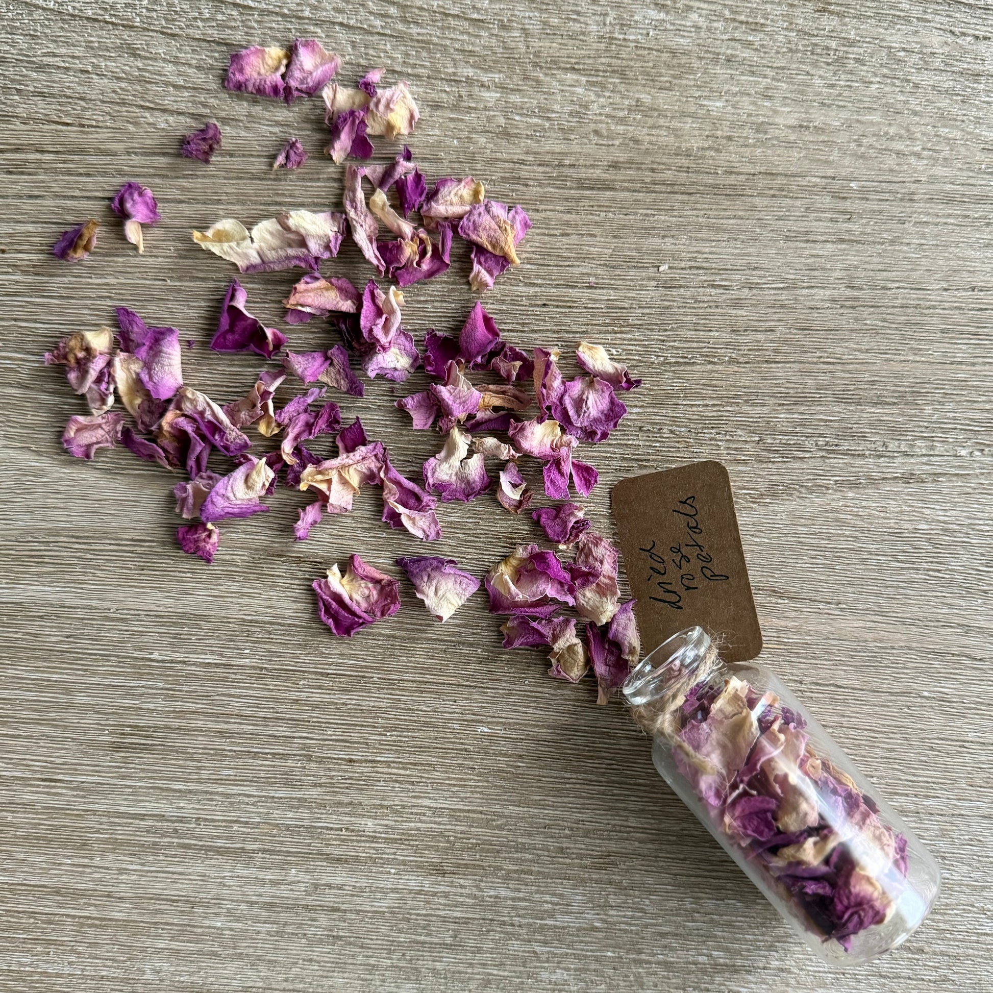 Small glass jar filled with dried purple and white flowers on a wooden surface.