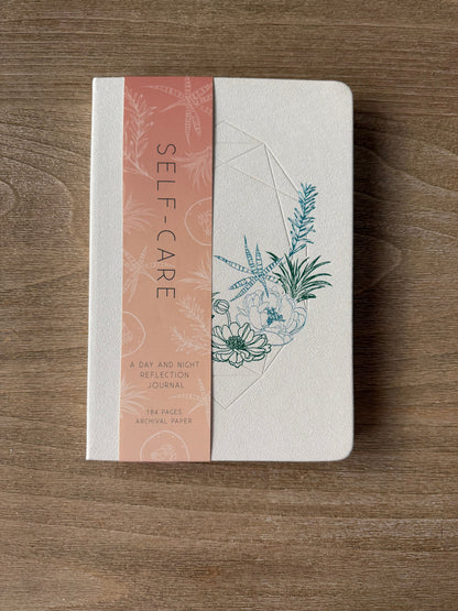 Notebook with a floral design on the cover and a pink band with text on a wooden surface