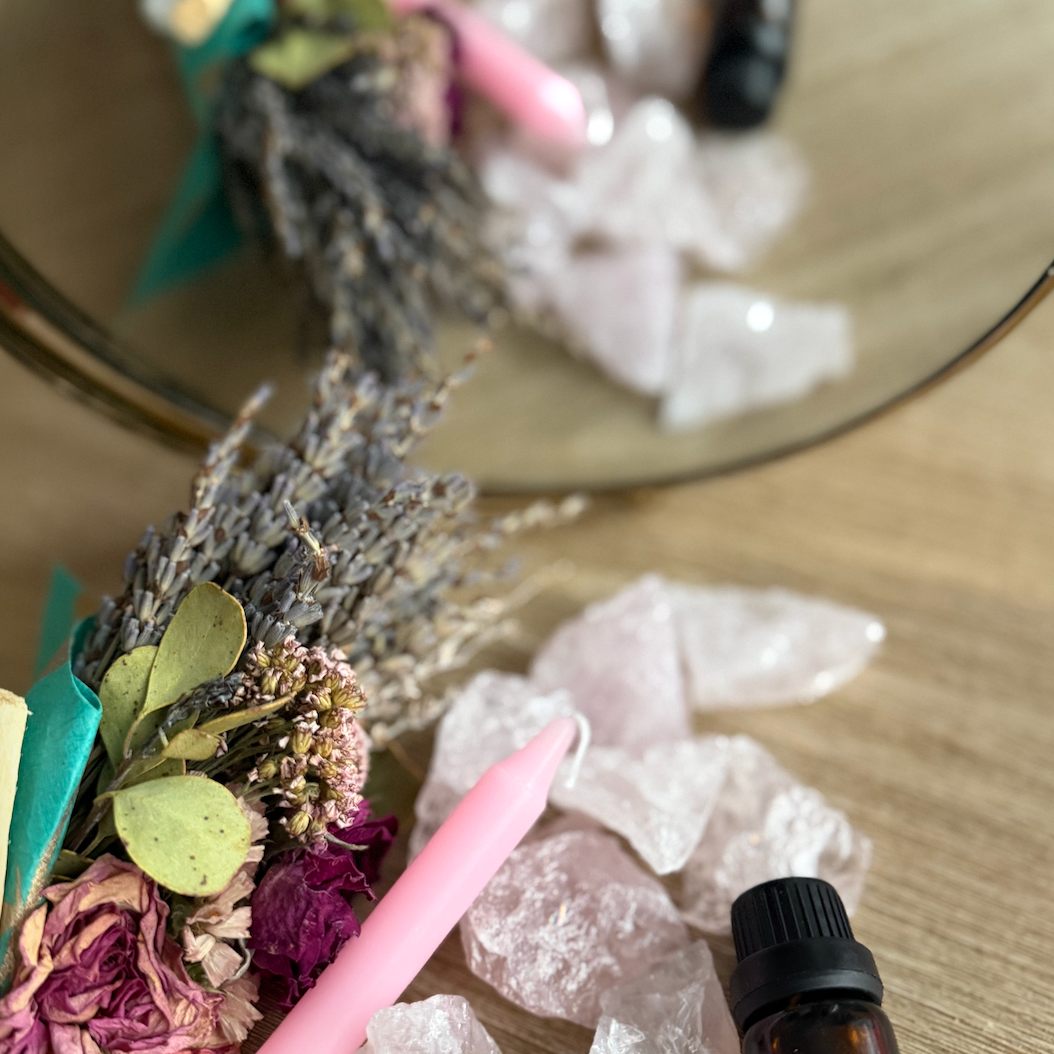 Crystal arrangement with flowers, a candle, and a bottle on a reflective surface.